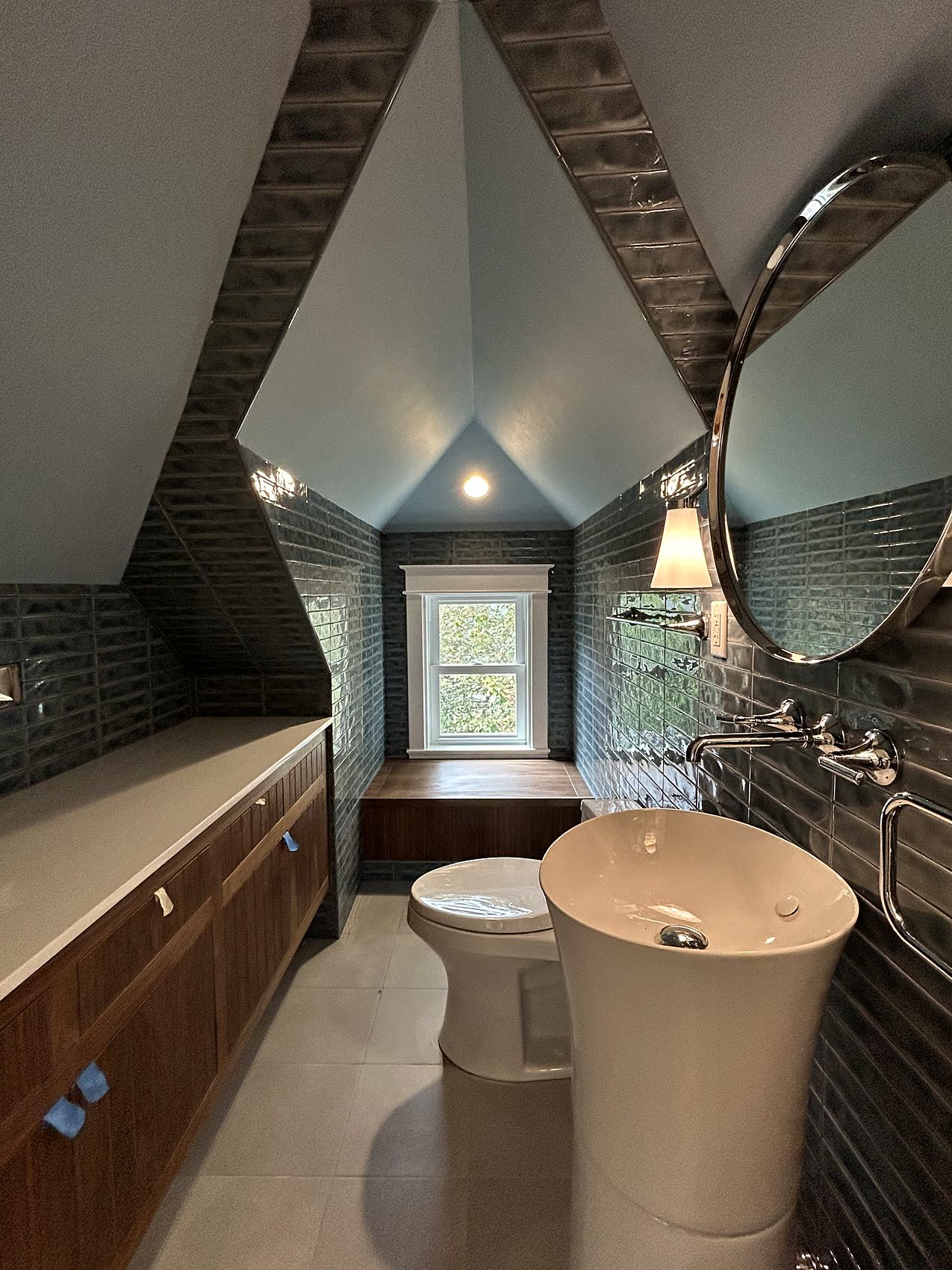 Attic bathroom with glossy teal tile, a pedestal sink, and a round mirror