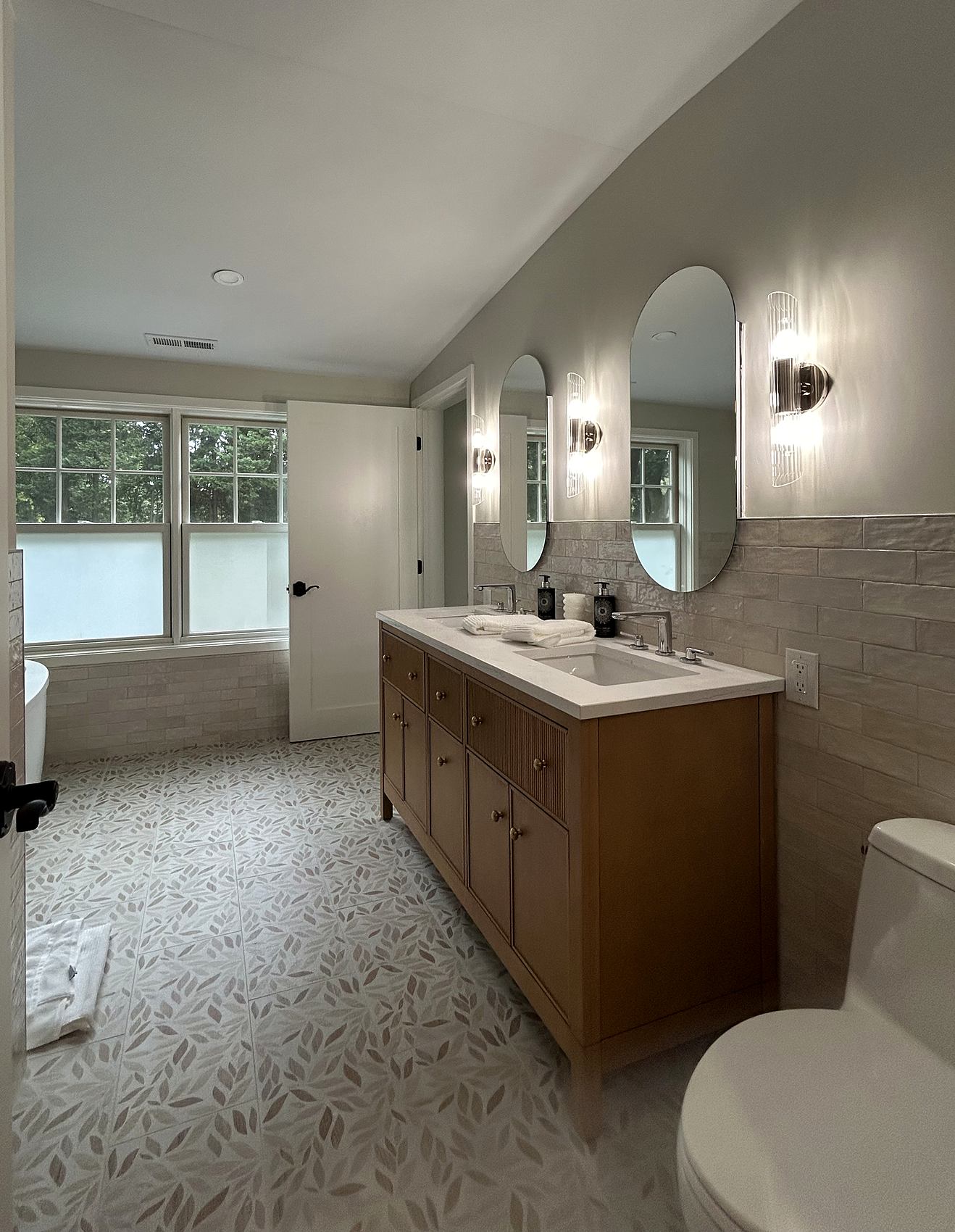 Bathroom with an oak double vanity, arched mirrors, and a leaf-pattern mosaic floor
