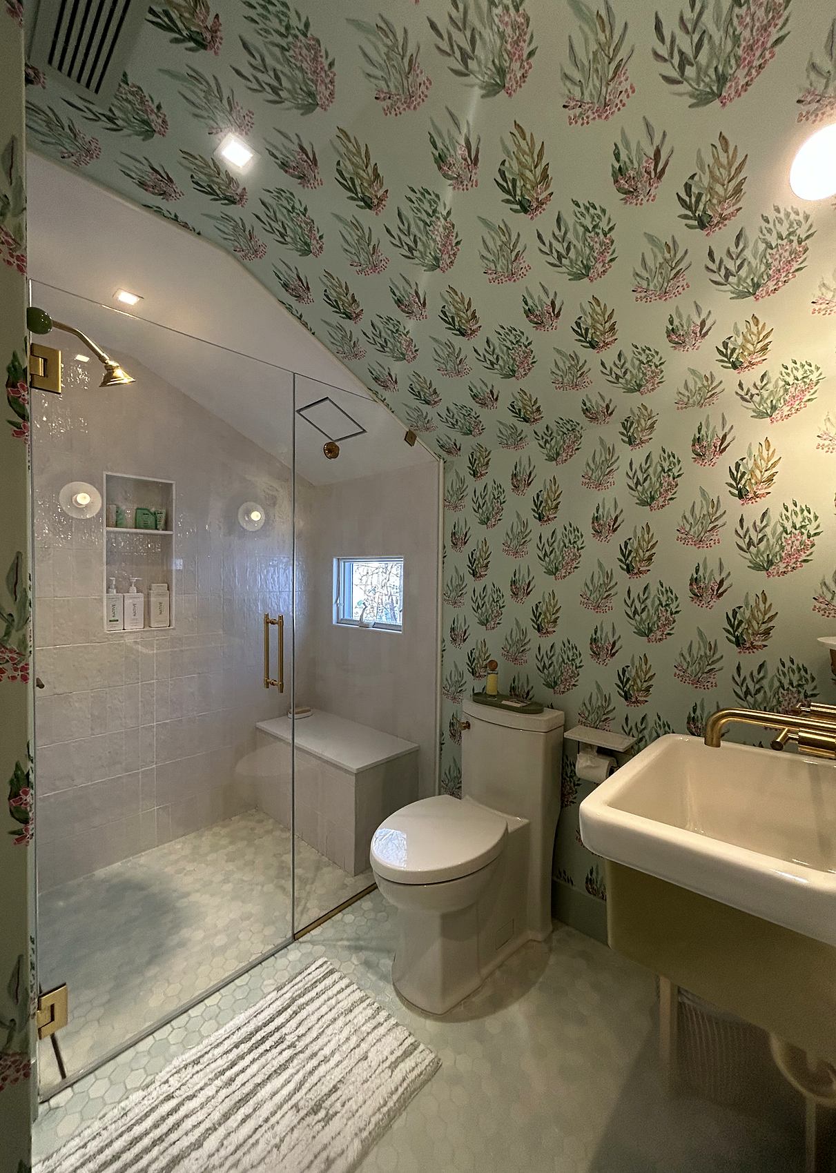 Bathroom with botanical wallpaper, a glass shower, and brass fixtures