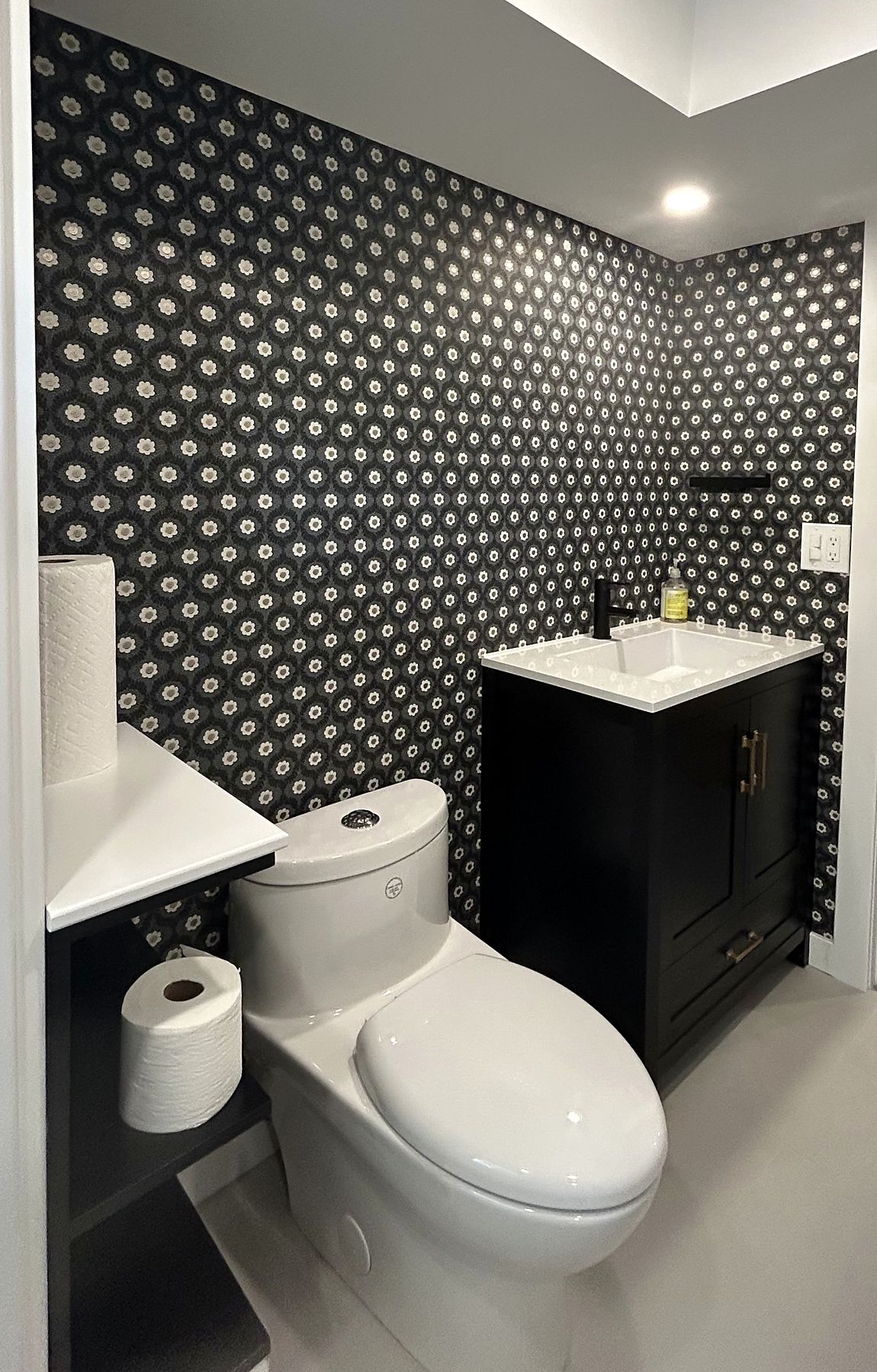 Powder room with patterned black wallpaper and a black vanity